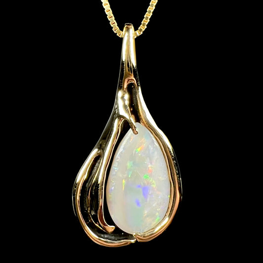 Close-up front view of a vintage 14k yellow gold opal solitaire pendant with Modernist design and black antiquing, shown on chain against black background