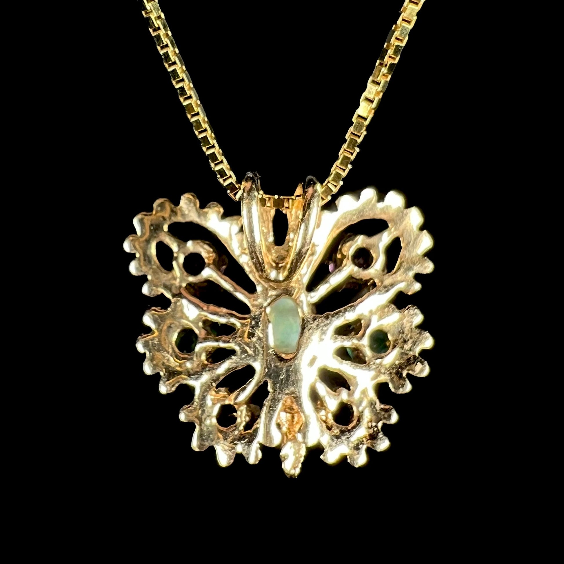 Back side of a vintage 14k yellow gold butterfly pendant on box-style chain against black background.