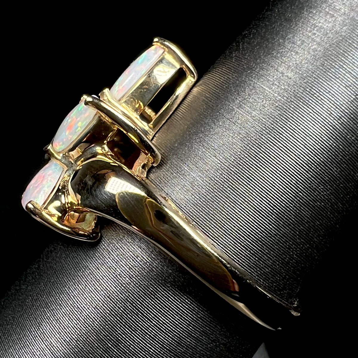 A vintage 14k yellow gold opal ring shown from the side view on a ring display; the sides of three opals are visible.