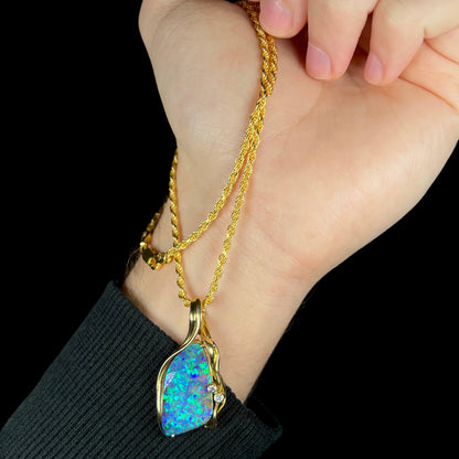 Hand dangling vintage 18k gold Australian boulder opal necklace from gold-tone rope chain. The pendant rests next to model's wrist.