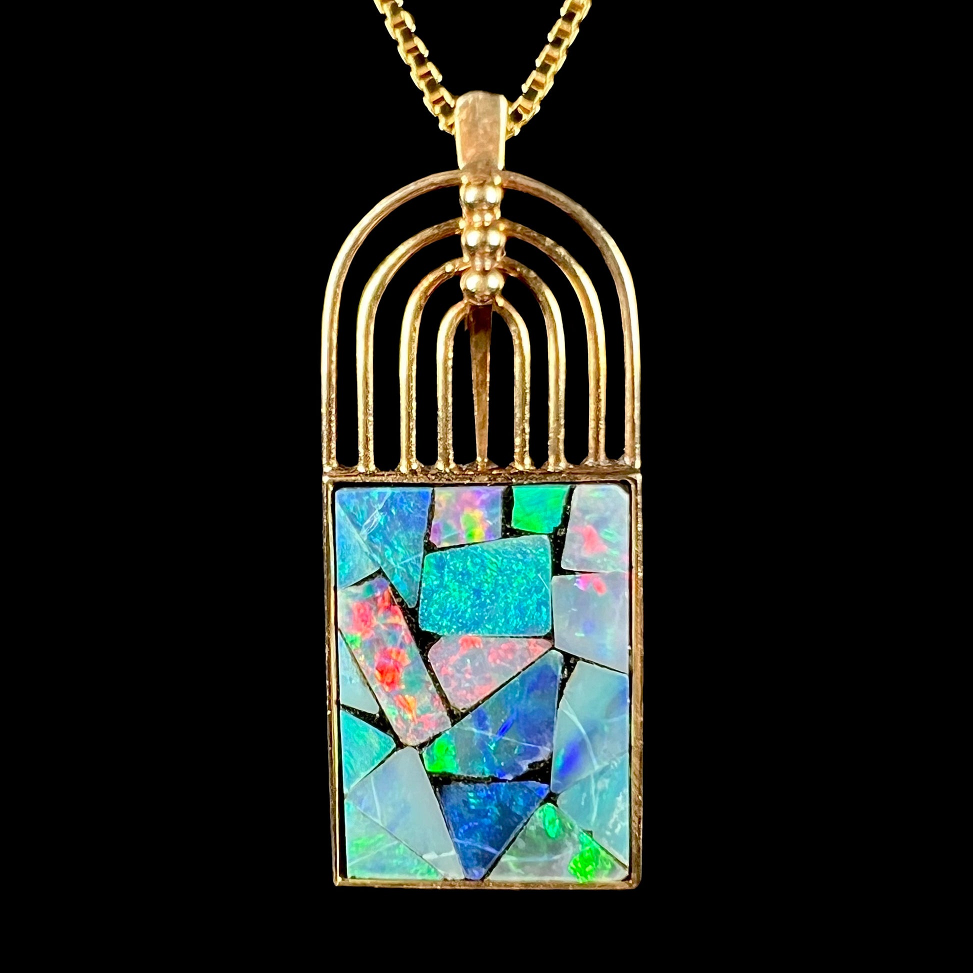 A vintage 18k gold mosaic opal necklace against a black background, with a bright red flash visible in the opal.