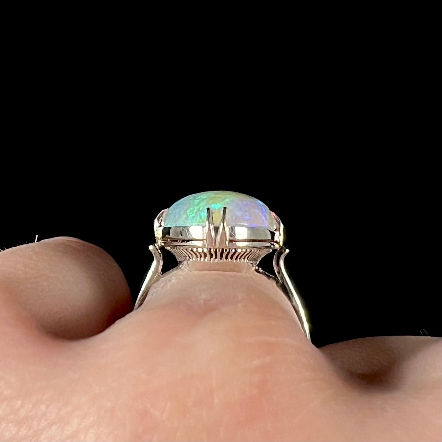 The gallery view of a vintage, 1950's-style opal ring worn on a finger.