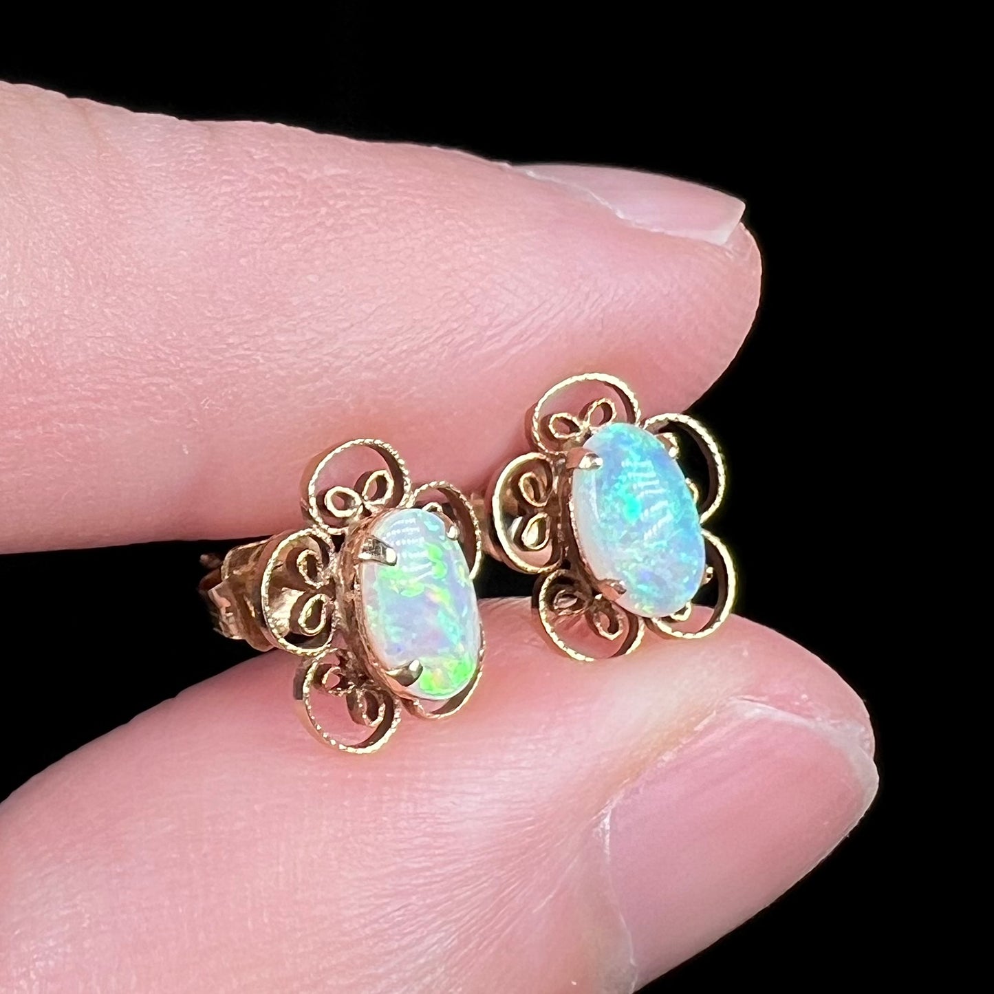 Angled close-up of vintage 1970s era opal flower earrings in 14k gold, held between two fingers