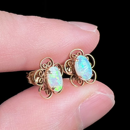 Angled close-up of vintage 1970s era opal flower earrings in 14k gold, held between two fingers
