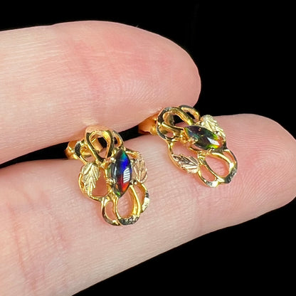 Vintage 1980s era gold lab-created black opal earrings shown close-up in fingers