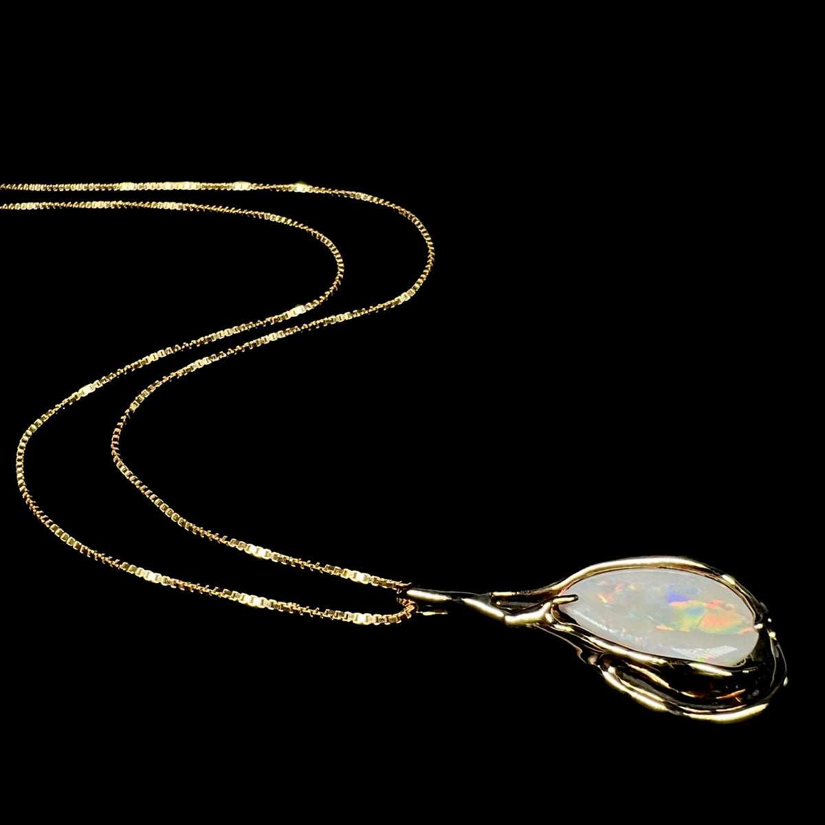 Vintage c.1980s era 14k gold Australian opal necklace shown from angle laying on black background, its chain flowing behind the pendant
