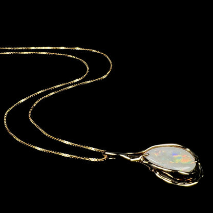 Vintage c.1980s era 14k gold Australian opal necklace shown from angle laying on black background, its chain flowing behind the pendant