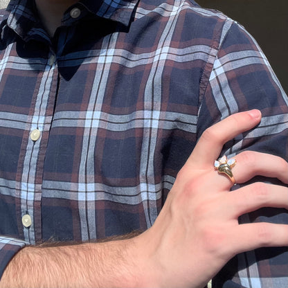 Person with plaid shirt wearing a vintage 1980s gold opal ring on hand in sunlight.  Their hand is resting on their opposing shoulder.