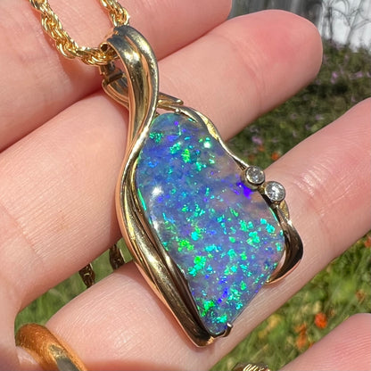 Angled macro view of vintage 1980s modernist gold pendant set with Australian boulder opal, held in hand under sunlight.