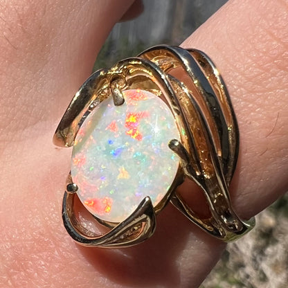 Red play-of-color seen shining across large Australian opal mounted in vintage c.1980s gold cocktail ring, worn on finger in sunlight