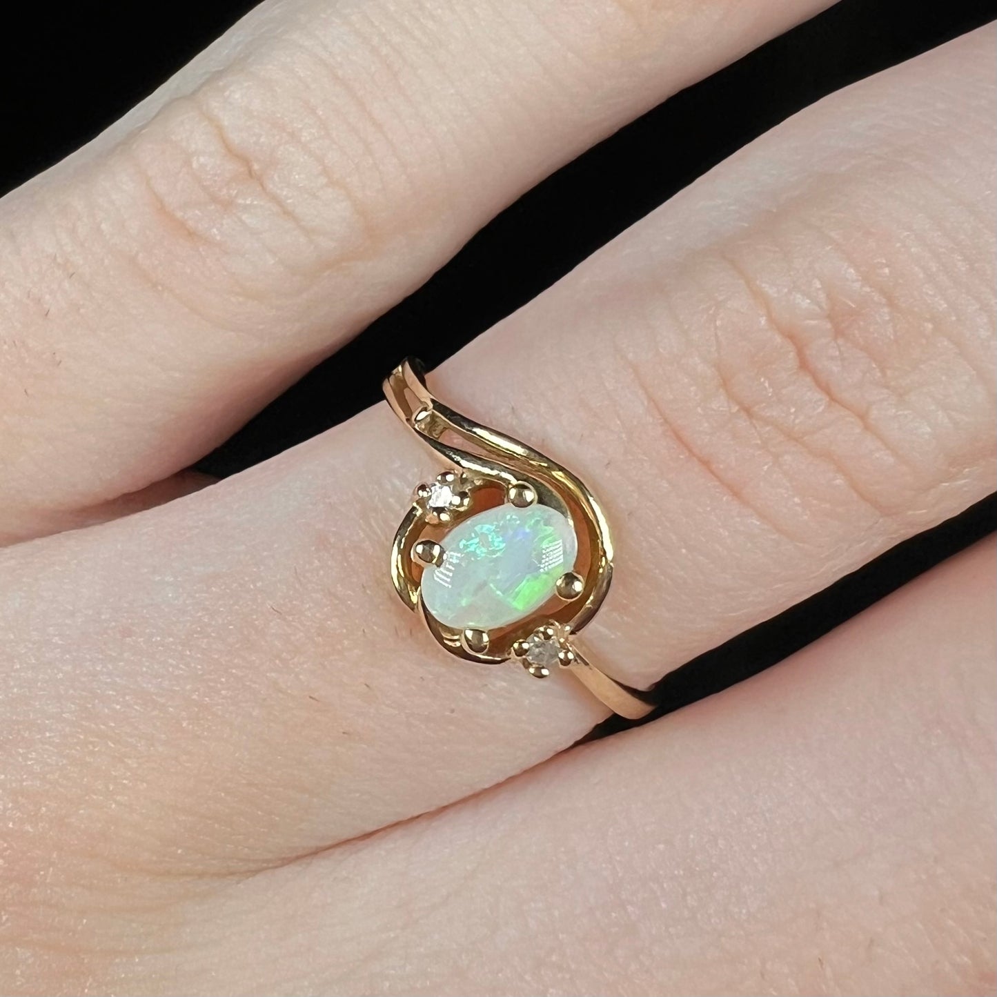 Close-up of a vintage 1990s 10k gold Australian opal and diamond engagement ring worn on a finger.