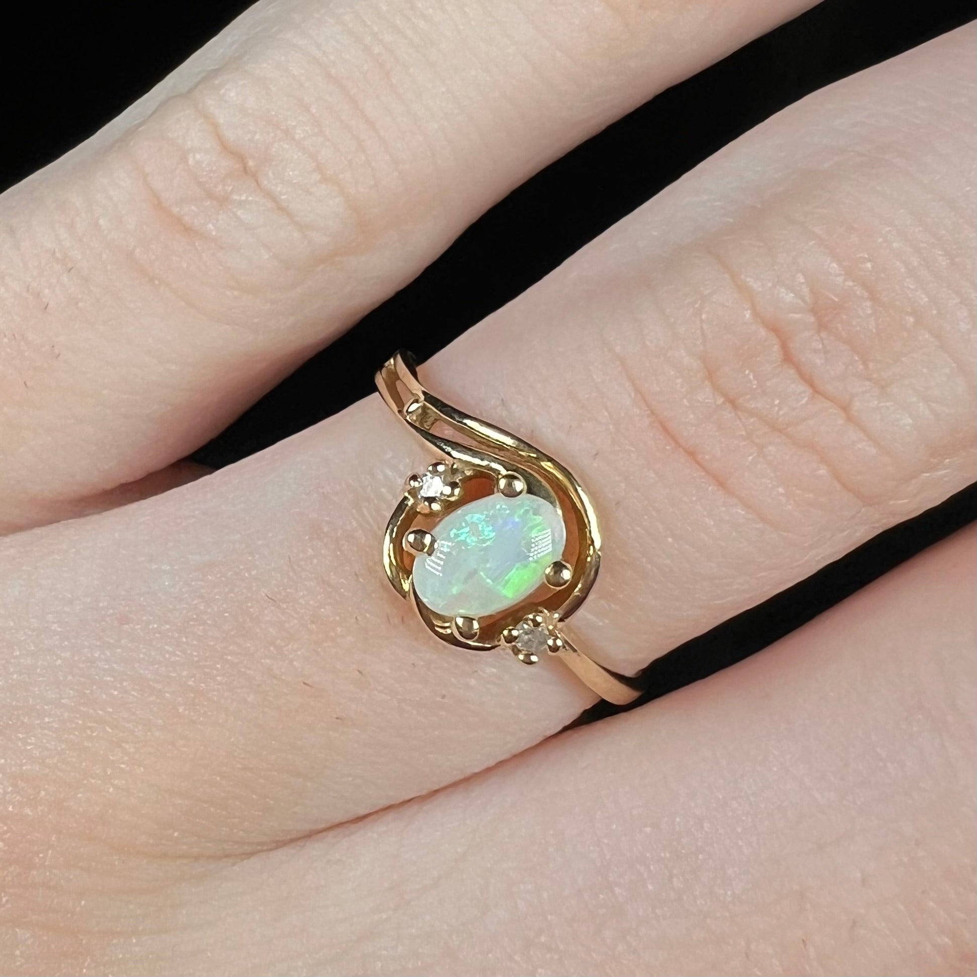 Close-up of a vintage 1990s 10k gold Australian opal and diamond engagement ring worn on a finger.