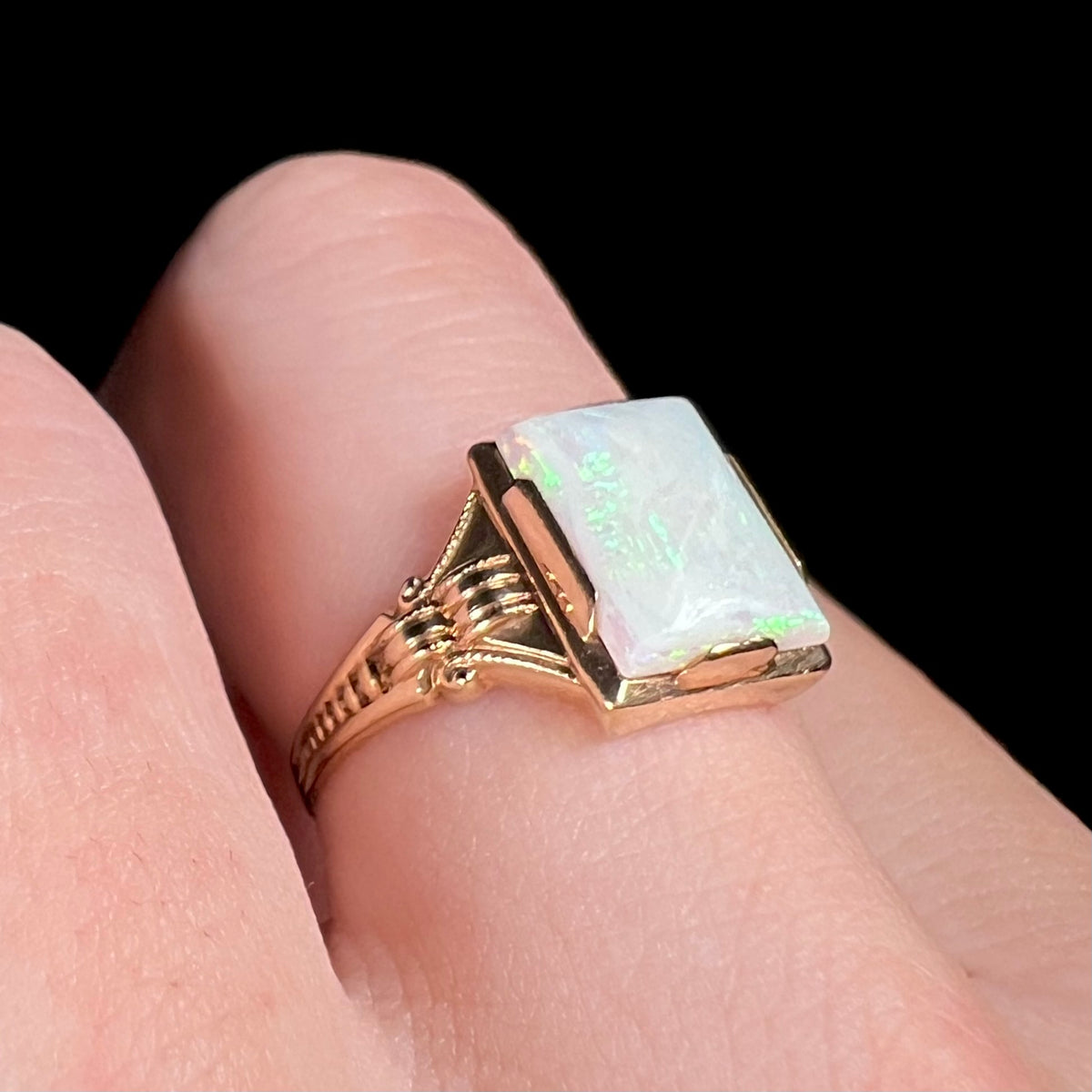Close-up of vintage Art Deco opal ring in 10k gold with ornate solitaire design, worn on finger and shown from angle