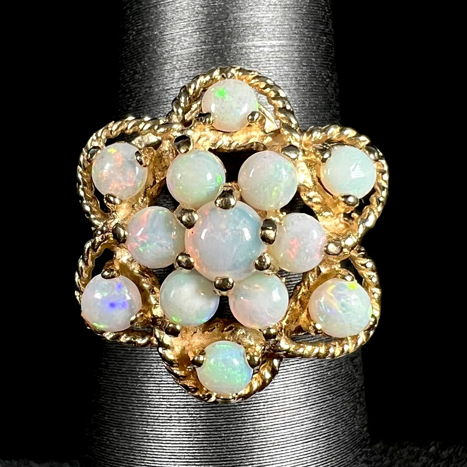 Close-up of a vintage, atomic-inspired opal cluster ring in yellow gold made by J.M. fox, shown on a ring display against a black background.