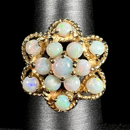 Close-up of a vintage, atomic-inspired opal cluster ring in yellow gold made by J.M. fox, shown on a ring display against a black background.