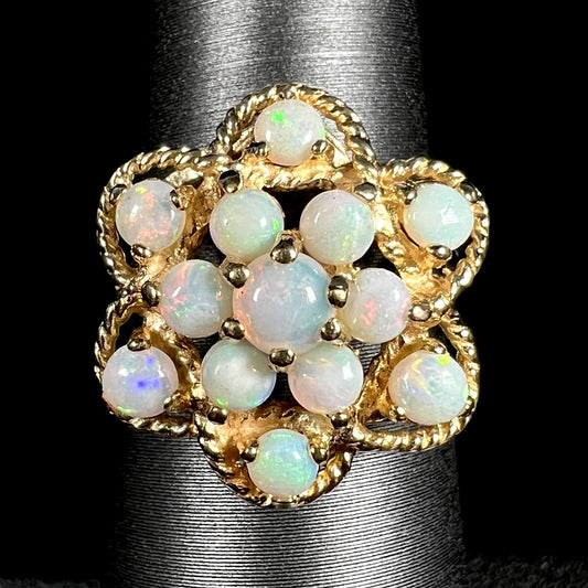 Close-up of a vintage, atomic-inspired opal cluster ring in yellow gold made by J.M. fox, shown on a ring display against a black background.