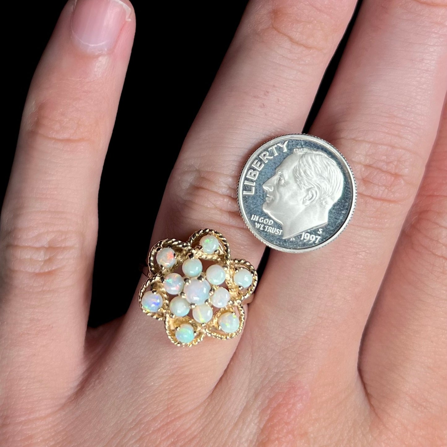 A vintage, yellow gold atomic opal cluster ring worn on a hand with a dime coin resting on the hand for scale.