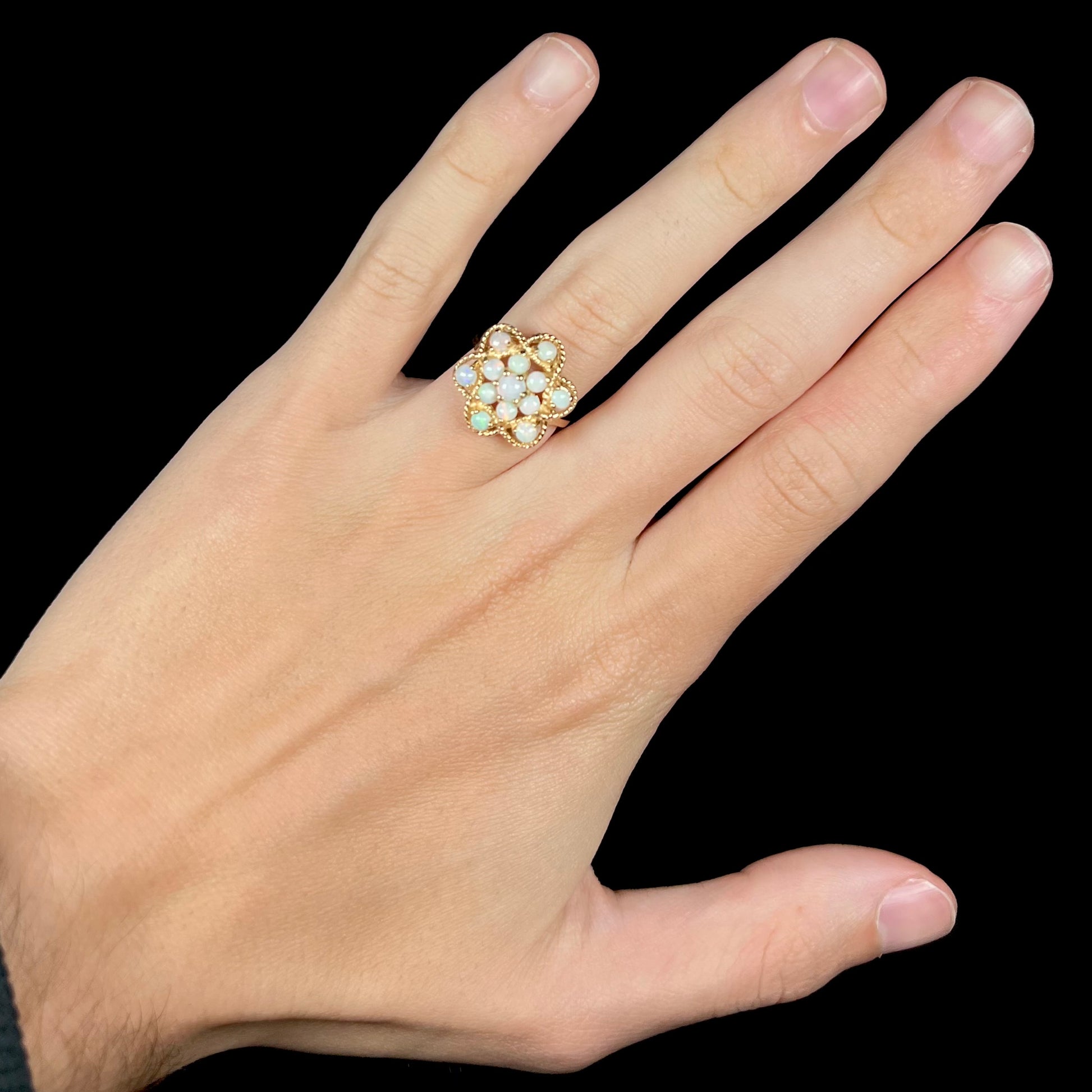 A hand wearing a vintage, yellow gold atomic-inspired Australian opal cluster ring against a black background.