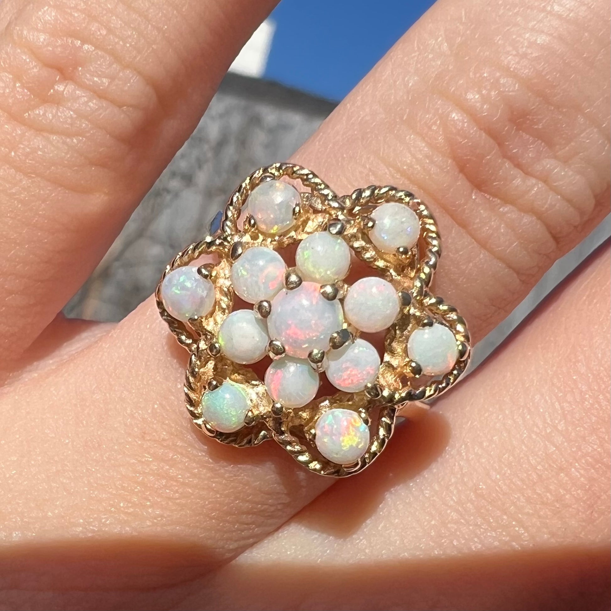Close-up of a vintage atomic-inspired Australian opal cluster ring in yellow gold, shown on a finger in the sunlight.