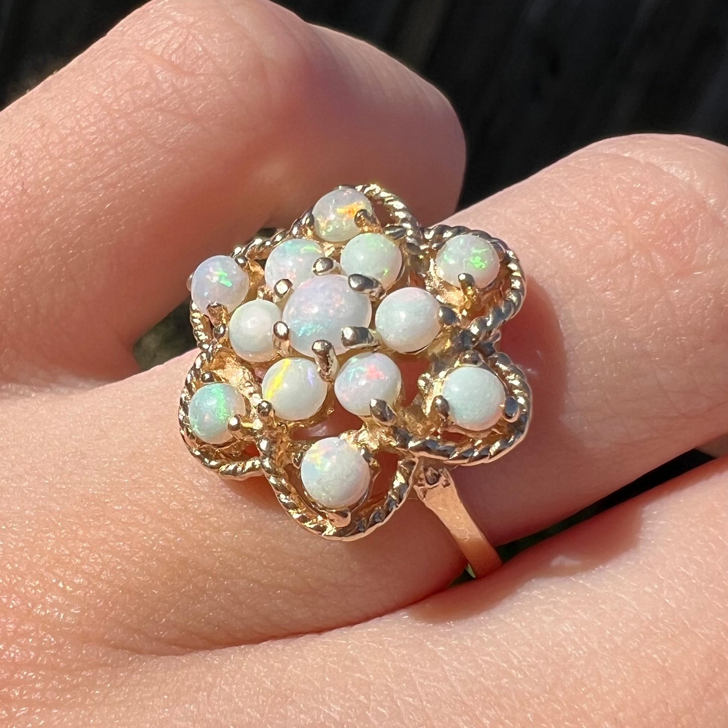 Angled, sunlit view of a vintage, USA-made opal cluster ring with an atomic motif, worn on a finger.