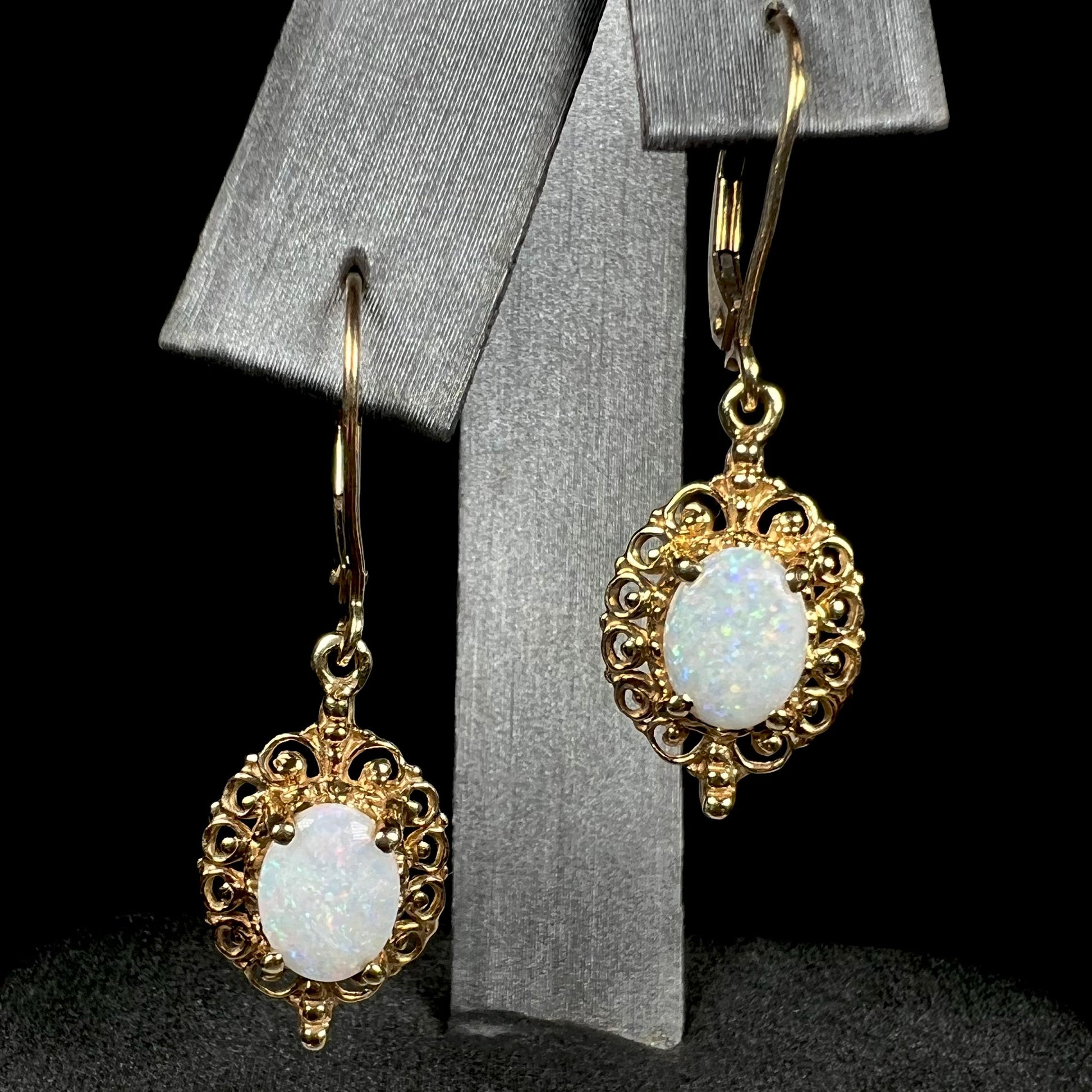 A pair of vintage yellow gold Australian light opal dangle earrings shown from the front view on an earring display.