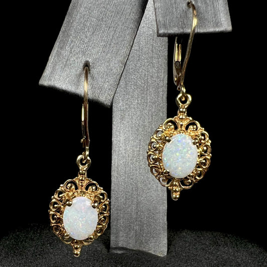 A pair of vintage yellow gold Australian light opal dangle earrings shown from the front view on an earring display.