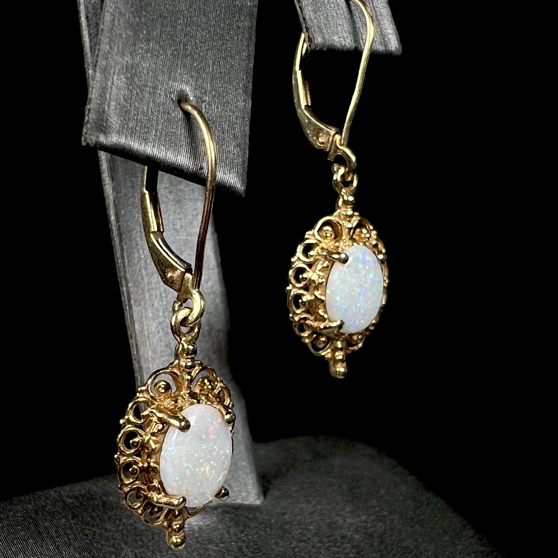 A pair of vintage yellow gold Australian light opal dangle earrings shown on an earring display from an angle.