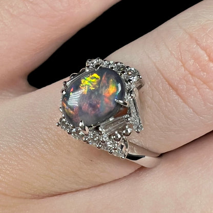Angled close-up of vintage c.1990s Australian opal engagement ring with diamond accents, worn on finger.  The ring has greenish yellow and orange play-of-color.
