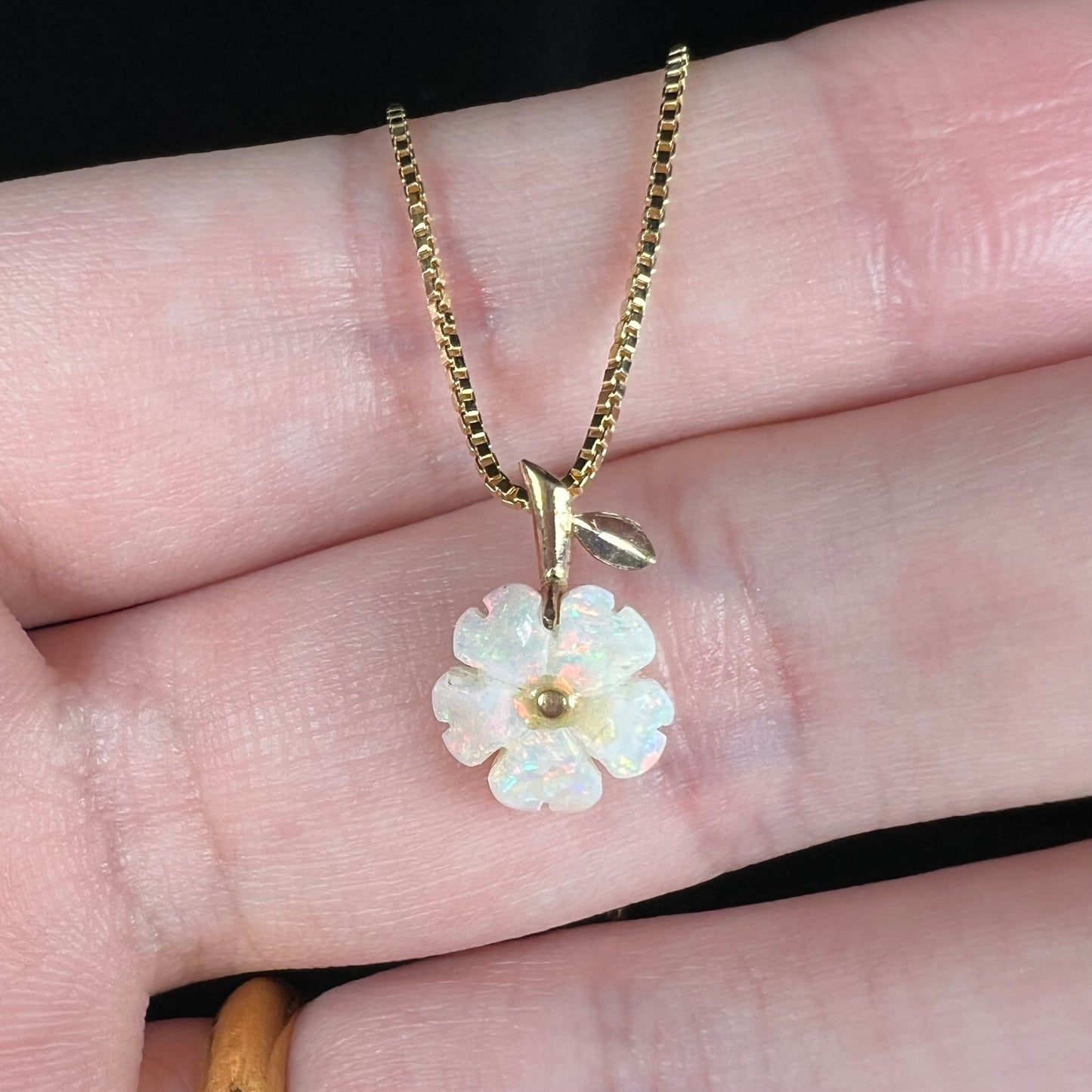 Close-up of a vintage Australian opal flower pendant shown held in a hand on a box-style chain under LED light.