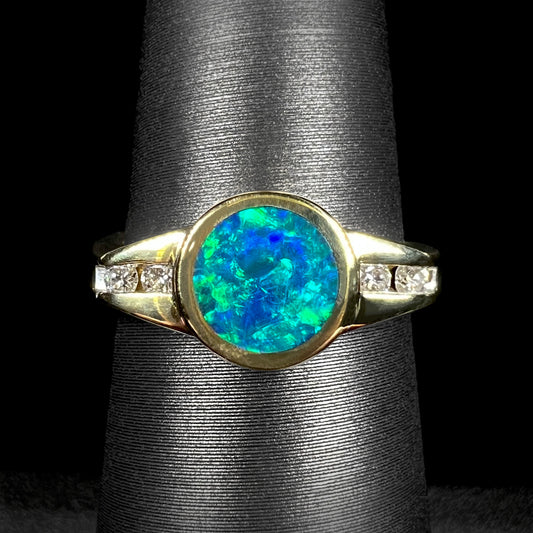 A vintage Australian black boulder opal engagement ring with green and blue fire, set in 18k yellow gold with diamonds by Luciano Bortone.  Studio lighting shows colors vividly.