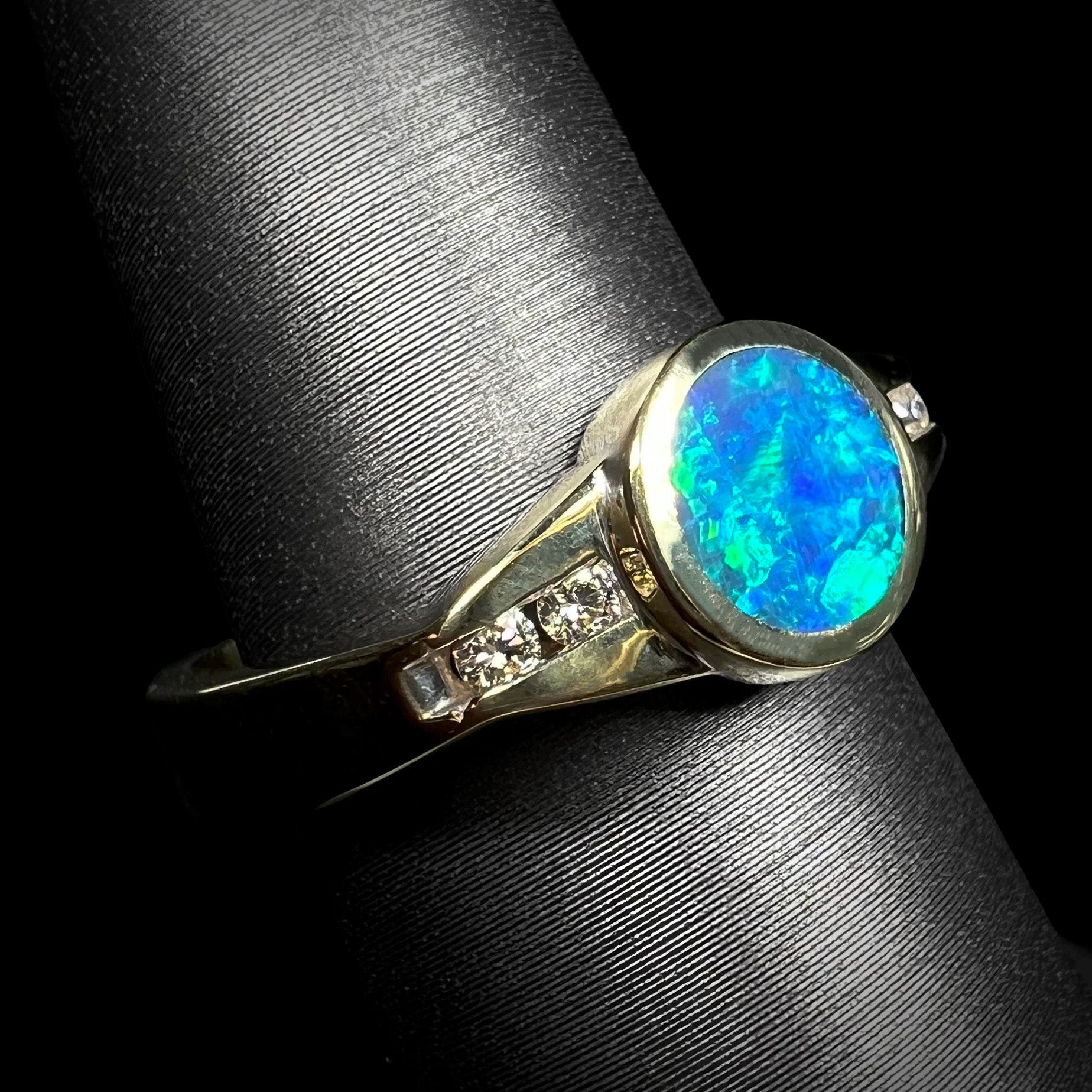 Angled close-up of a vintage, unisex boulder opal and diamond ring with green-blue color play, displayed on a ring mount.