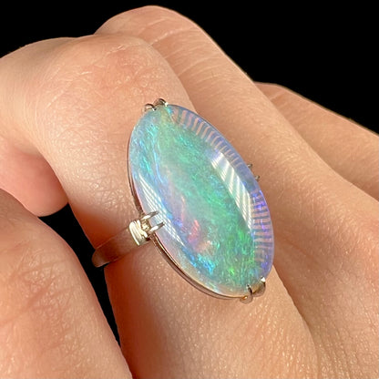 A vintage, 1950's-era crystal opal ring worn on a finger.  Soft green and purple colors are seen in the opal.