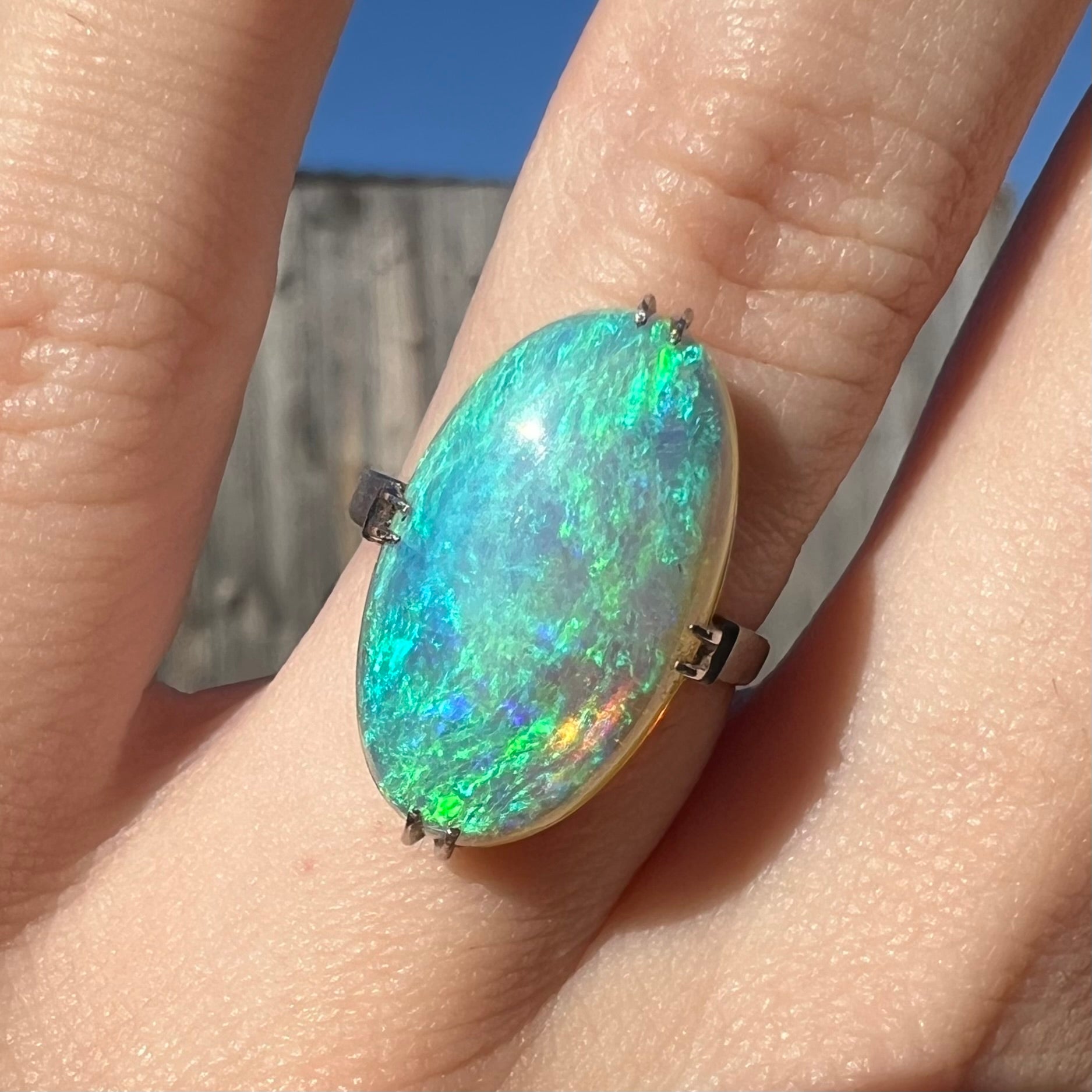 A vintage crystal opal ring worn in the sunlight, showcasing teal and green color play.