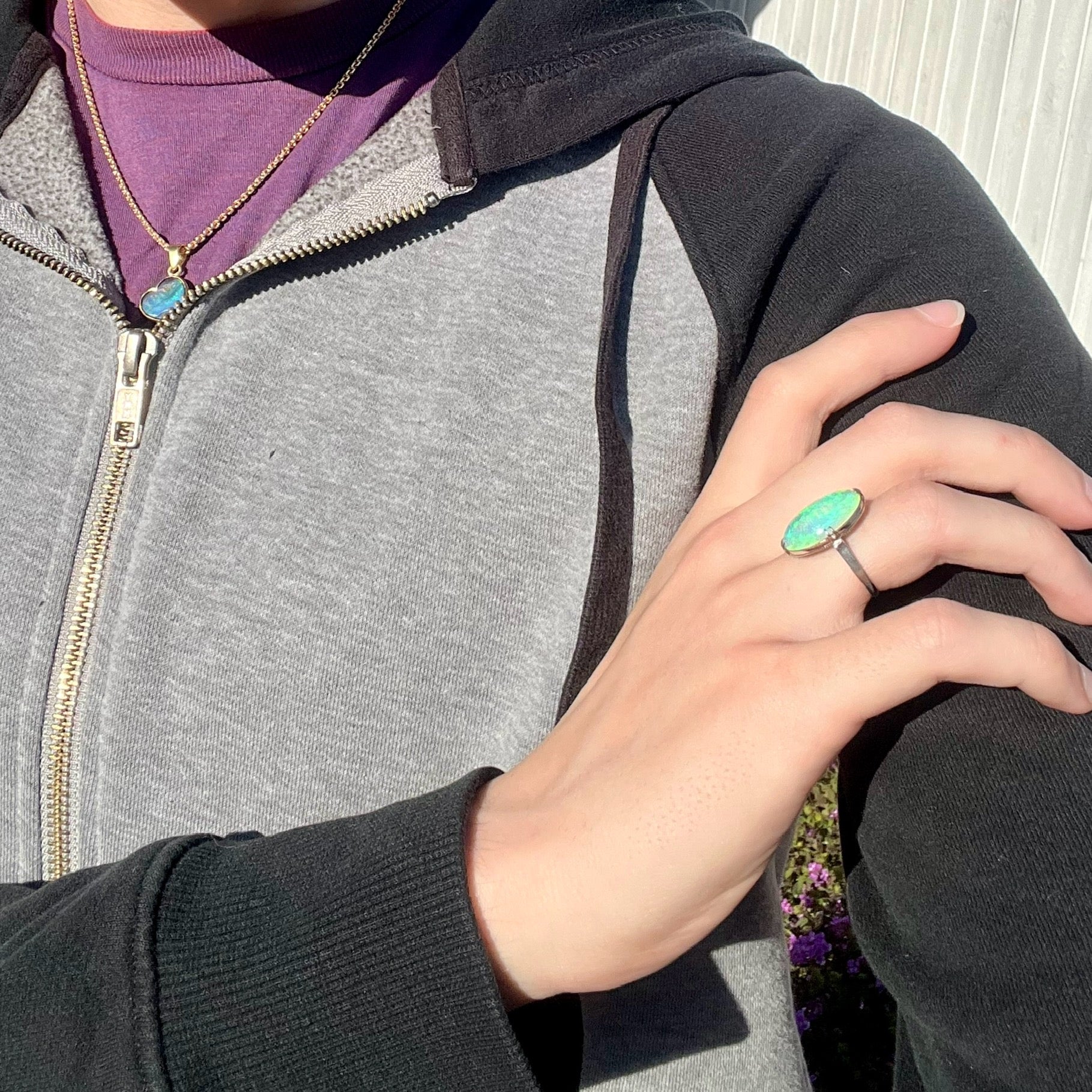 A vintage crystal opal solitaire ring worn on a model's hand in the sunlight.  The opal is green.