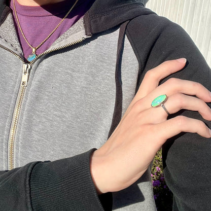 A vintage crystal opal solitaire ring worn on a model's hand in the sunlight.  The opal is green.