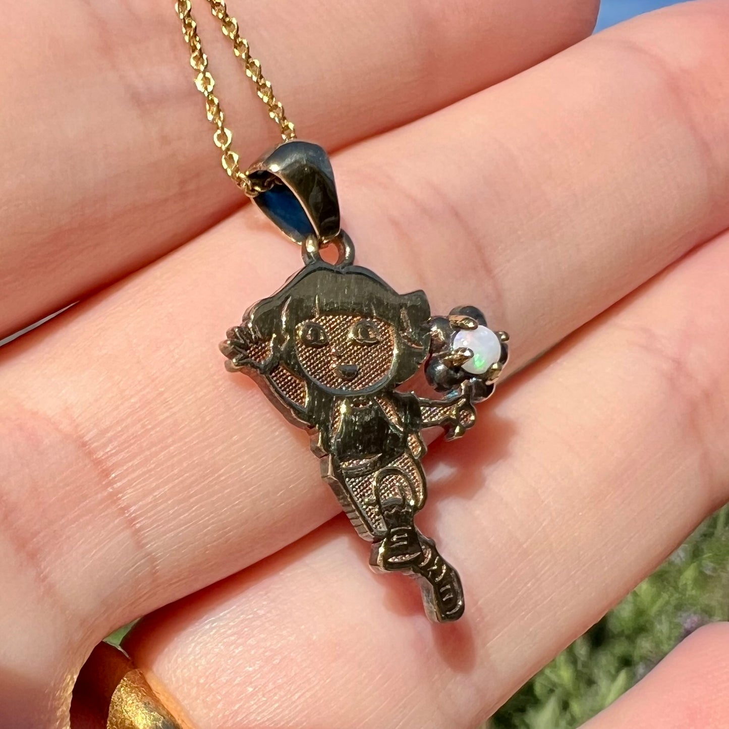 Angled close-up of vintage Dora the Explorer opal necklace held in a hand in sunlight.  The Australian opal has green play of color.