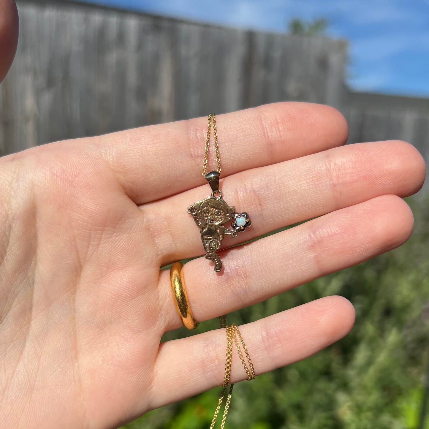 Hand holding vintage 2009 Dora the Explorer gold-tone sterling silver opal necklace in natural sunlight against outdoor backdrop.