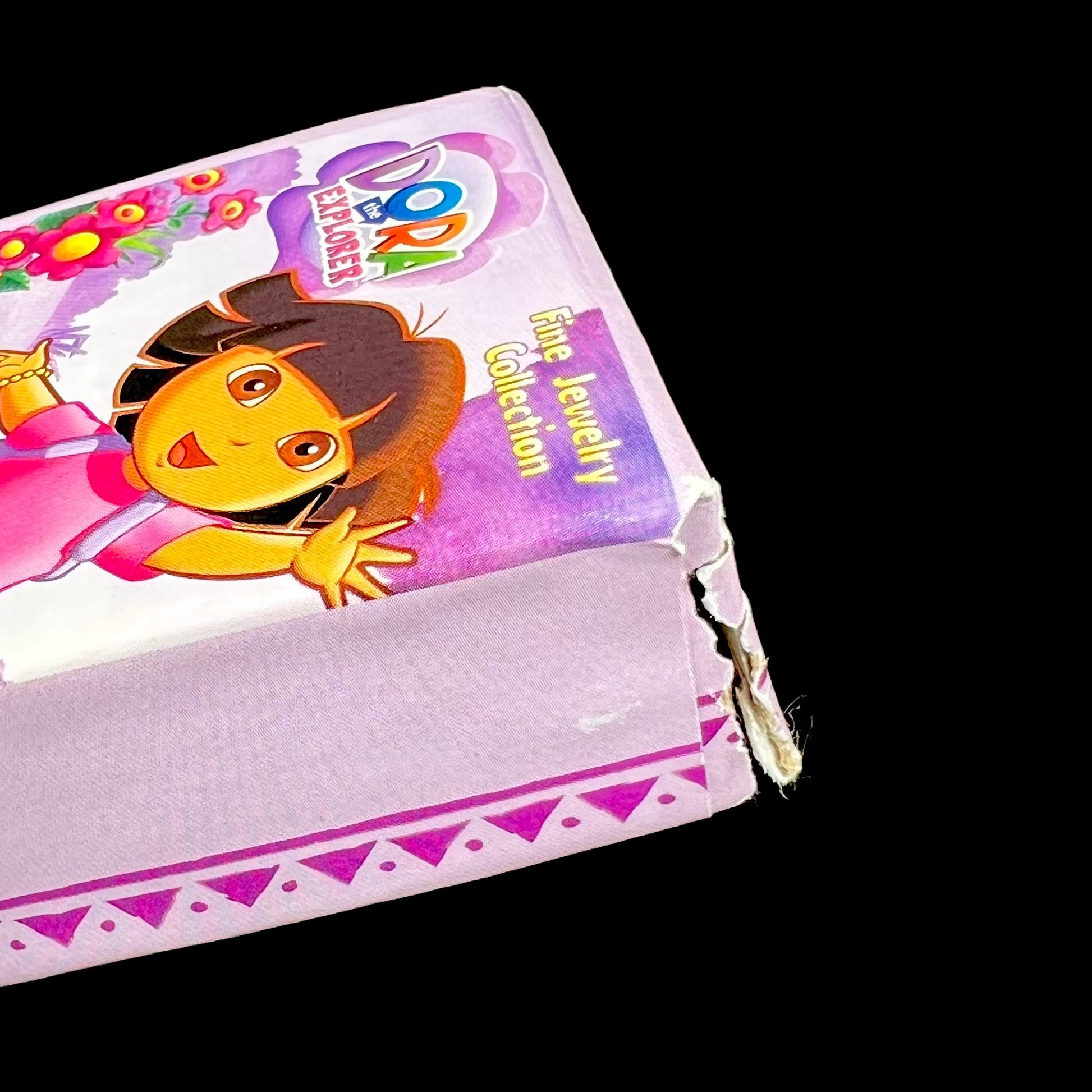 Dora the Explorer Fine Jewelry Collection packaging with rip on corner of box against a black background.