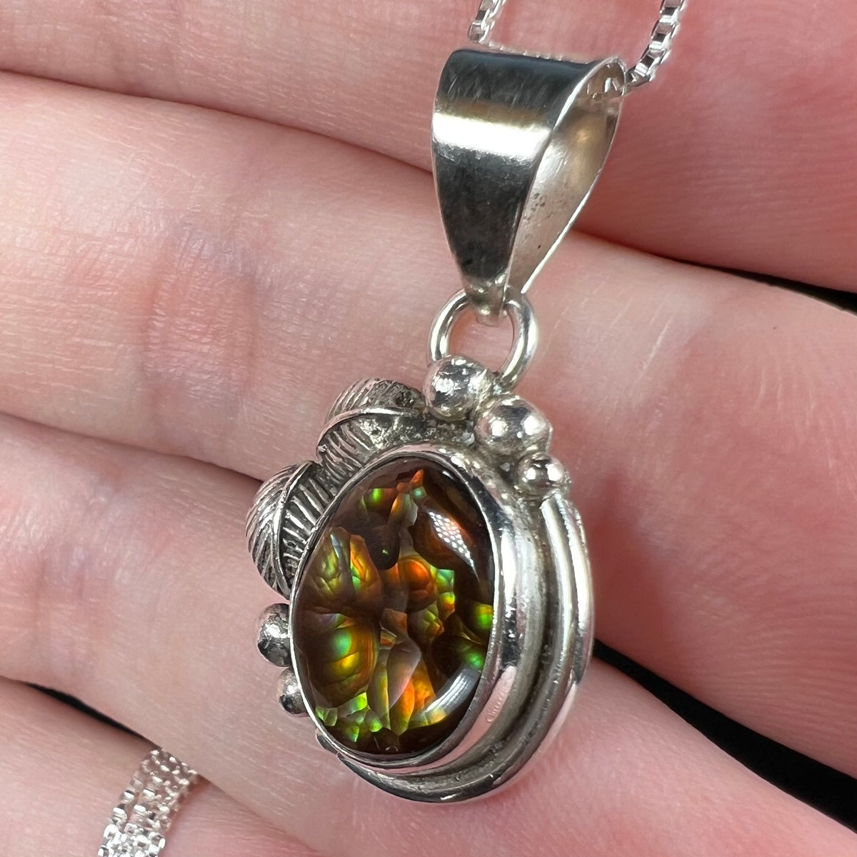 A vintage fire agate pendant with handmade sterling silver unisex setting, shown from angle close-up in hand on chain.