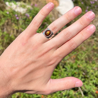 A vintage, silver unisex fire agate ring, worn on a hand in the sunlight against an outdoor backdrop.