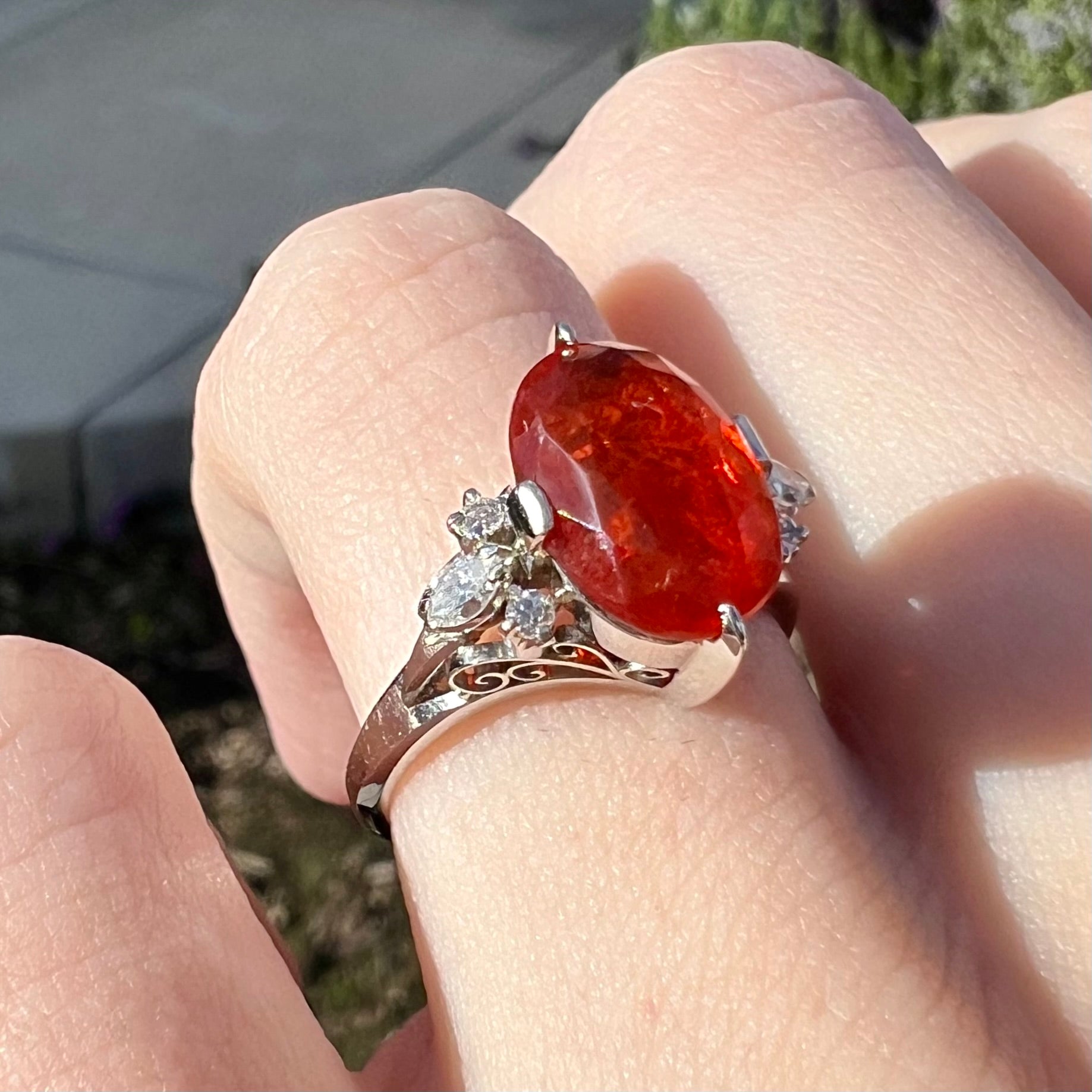 A vintage, Japanese Mid-Century style platinum fire opal and diamond ring worn on a hand.  Filigree designs can be seen.