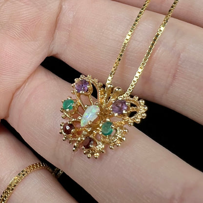 A vintage gold and multi-gemstone butterfly pendant with a 1960s era gear design, shown close-up in a hand from an angle.