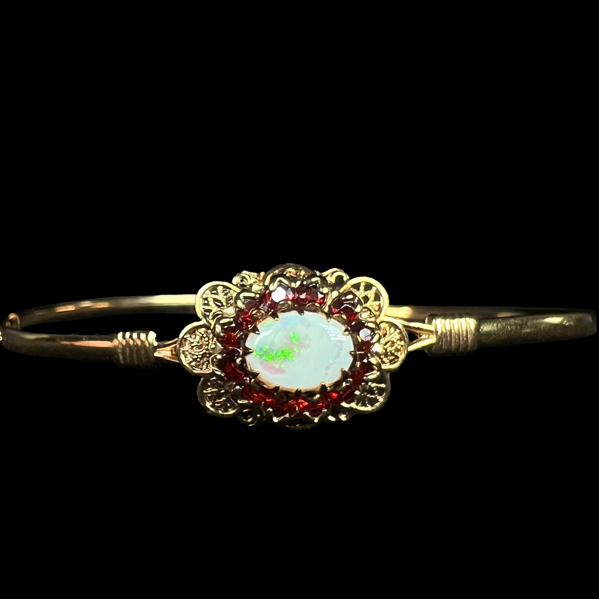 A vintage yellow gold Australian opal and garnet halo bangle bracelet shown against a black background.