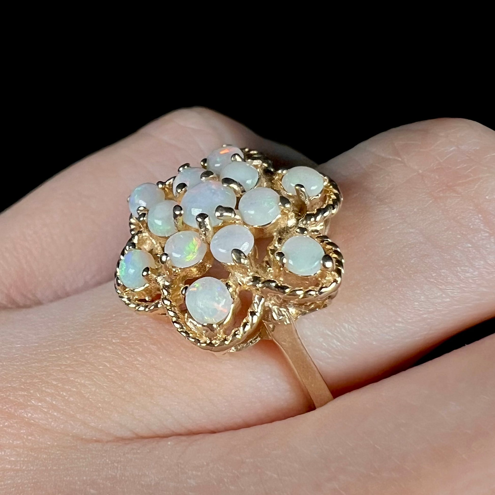 A vintage yellow gold opal cluster ring with an atomic-inspired motif, shown from an angle close-up on a finger.