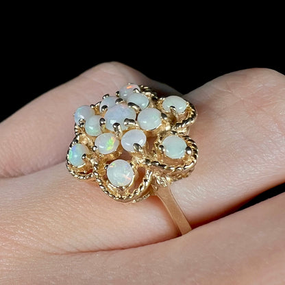 A vintage yellow gold opal cluster ring with an atomic-inspired motif, shown from an angle close-up on a finger.