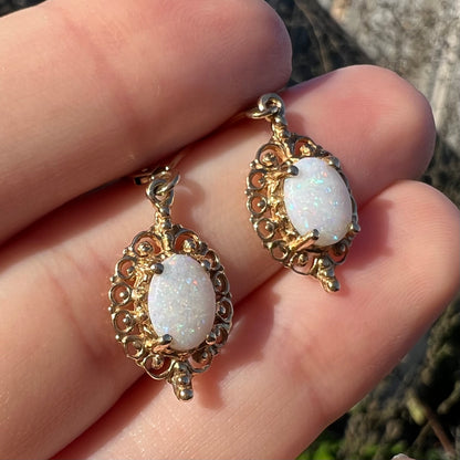 Close-up angled sunlit view of a pair of vintage yellow gold Australian light opal dangle earrings shown in a hand.
