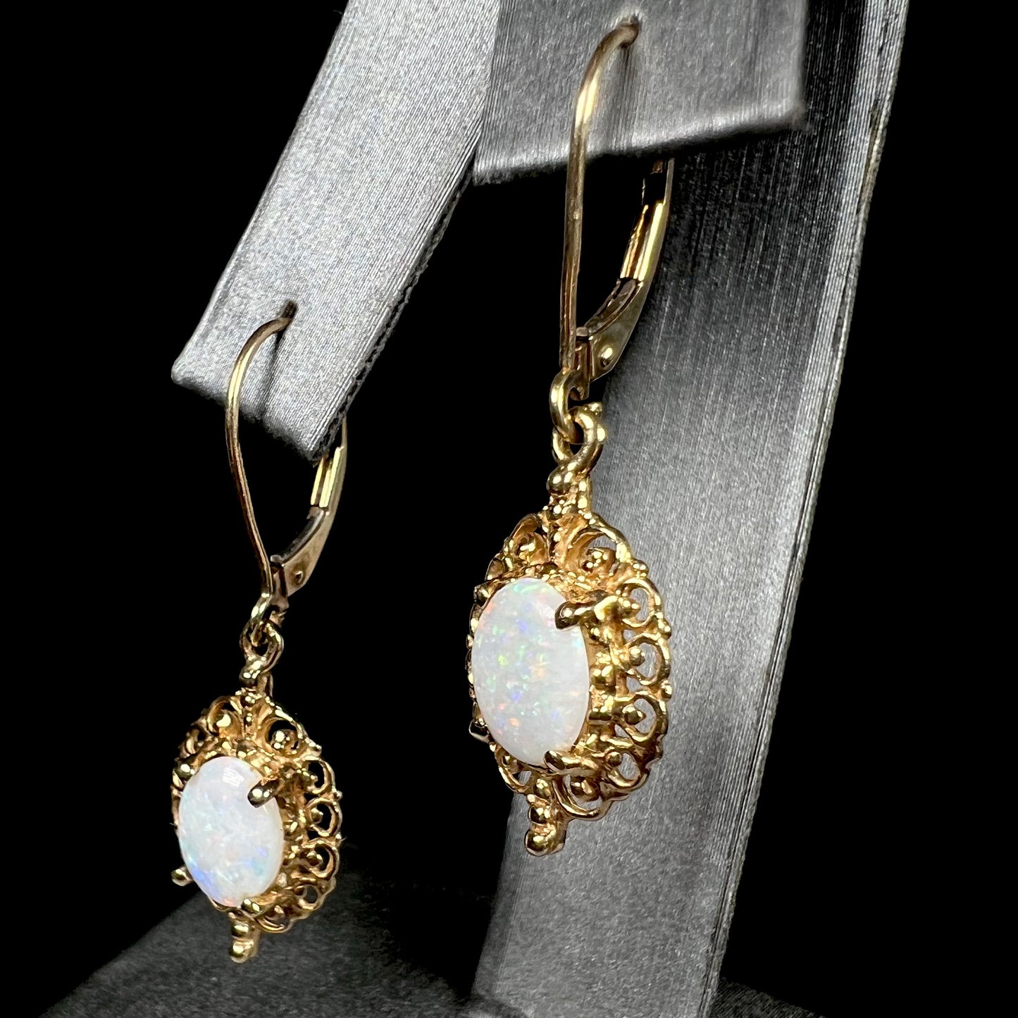 Angled view of a pair of vintage yellow gold Australian light opal dangle earrings shown on an earring display