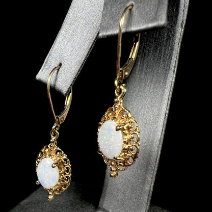 Angled view of a pair of vintage yellow gold Australian light opal dangle earrings shown on an earring display