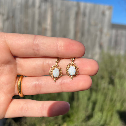 A pair of vintage yellow gold Australian light opal dangle earrings shown in the sunlight held in a hand.