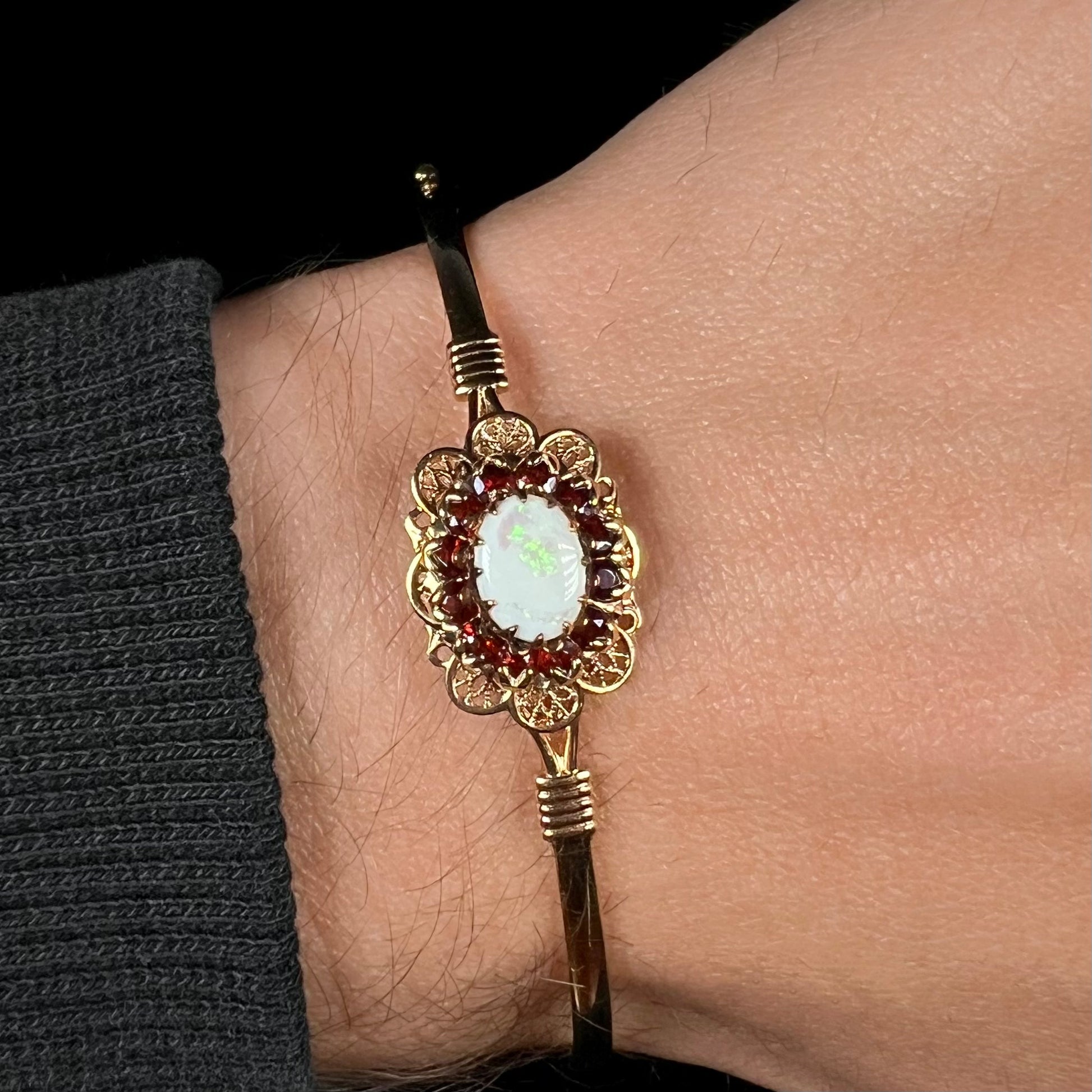 A vintage yellow gold Australian opal and garnet halo bangle bracelet shown close-up on a wrist.